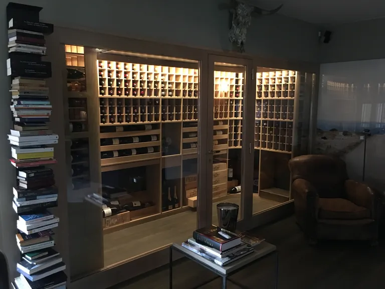 Cava de vivienda con botelleros de roble macizo llenos de botellas y luz cálida indirecta